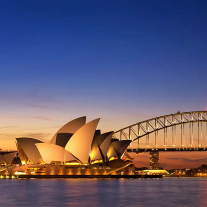 Australien – Utsikt över Operahuset i Sydney i skymningen, med en färgsprakande himmel och belysning på bron.