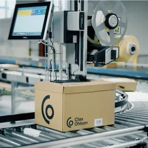 En kartong märks på ovansidan av den automatiska etiketteringsmaskinen MPERIA A-Series på en produktionslinje.