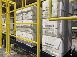 Stora produktkuber inslagna i vitt papper på ett transportband. Kuberna har märkts med QR-koder och alfanumeriska tecken i svart bläck.
