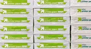 Staplar med förpackat skrivarpapper i Letter-format med gröna och vita etiketter, uppställda i rader.
