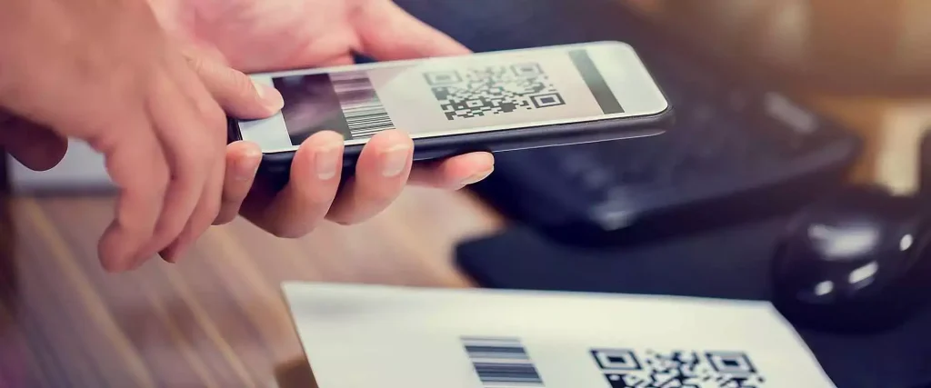 En person som håller en smartphone där en 2D-QR-kod och en traditionell 1D-streckkod visas ovanför en produktförpackning där båda streckkodsformaten finns.