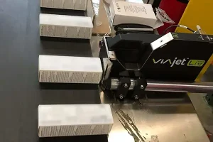 Matthews Marking Systems VIAjet L12, en termisk Bläckstråle -skrivare som märker vita produktkartonger medan de rör sig längs ett produktionsband.